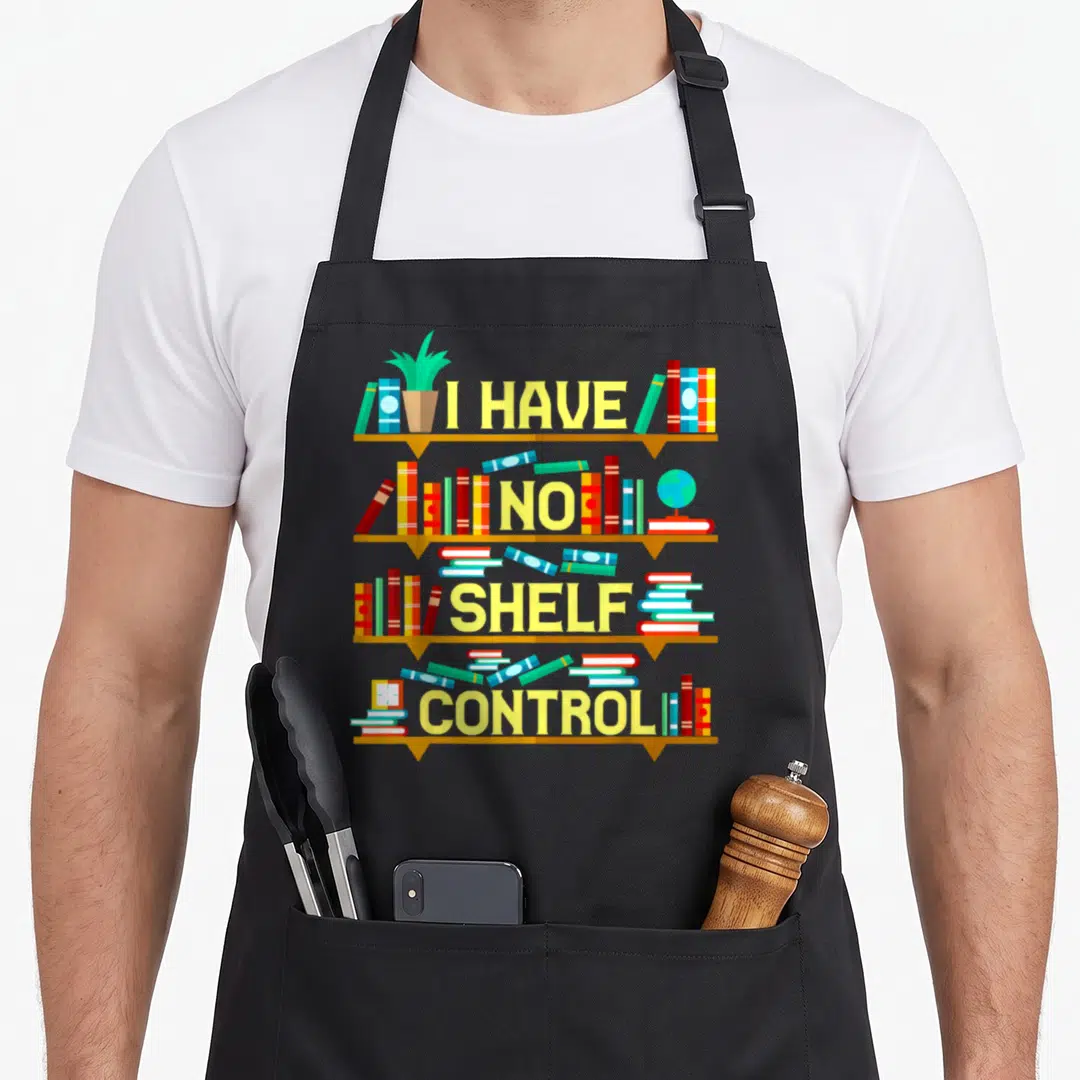 Pun book apron - Four brown shelves with books and yellow text reading I HAVE NO SHELF CONTROL — shown on a black cotton canvas apron against a white background