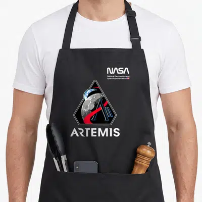 Artemis nasa apron - Triangular emblem with moon earth and stylized A above white ARTEMIS text and NASA logo — shown on a black cotton canvas apron against a white background