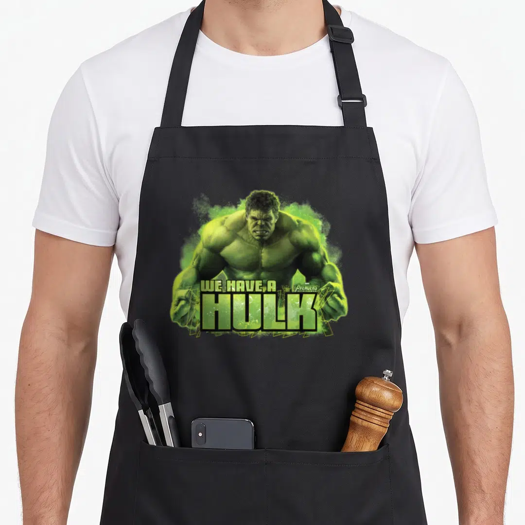 Funny war infinity apron - Green Hulk illustration with We Have A Hulk text and Avengers logo overlay — shown on a black cotton canvas apron against a white background