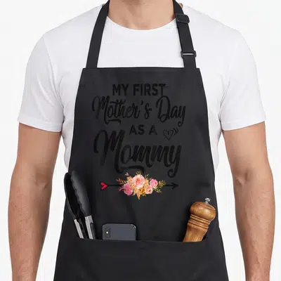 Mother's day aprons for women - Black text My First Mother's Day as a Mommy with pink flowers and red heart arrow — shown on a black cotton canvas apron against a white background