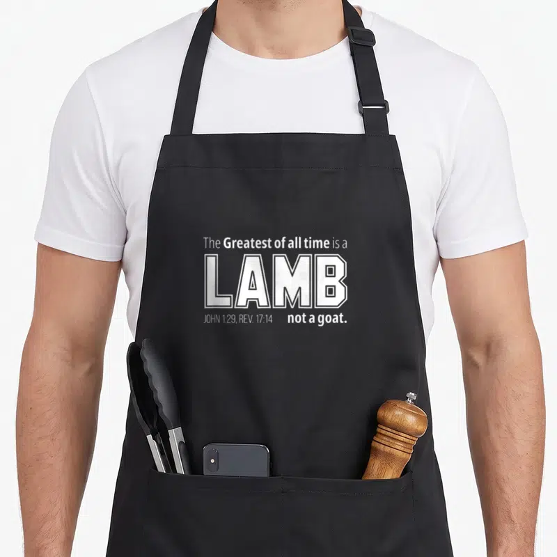 Lamb goat apron - White stacked text reading The Greatest of all time is a LAMB not a goat with scripture references — shown on a black cotton canvas apron against a white background