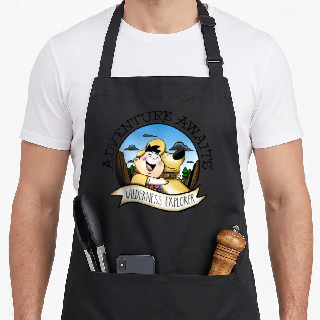 Dug explorer apron - Cartoon boy hugging dog in circle with adventure awaits text and wilderness explorer banner — shown on a black cotton canvas apron against a white background