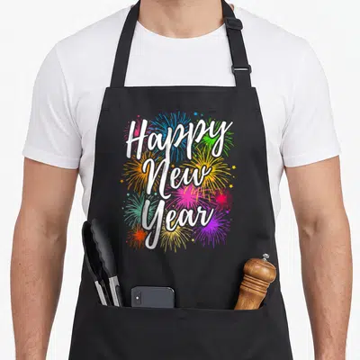 Funny supply eve apron - White Happy New Year text over blue pink yellow green and white fireworks — shown on a black cotton canvas apron against a white background