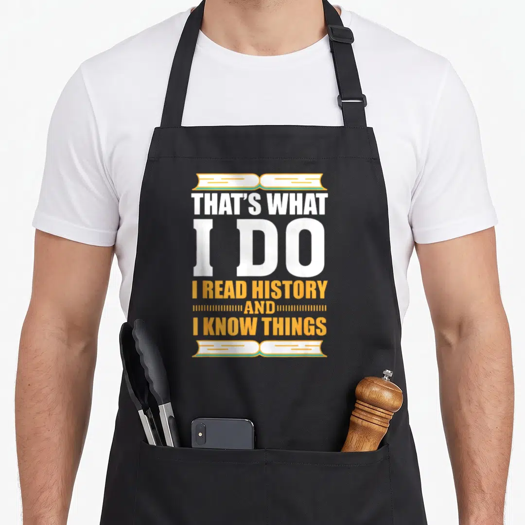 Buff teacher apron - Stacked white and orange text reading I read history flanked by open book illustrations — shown on a black cotton canvas apron against a white background
