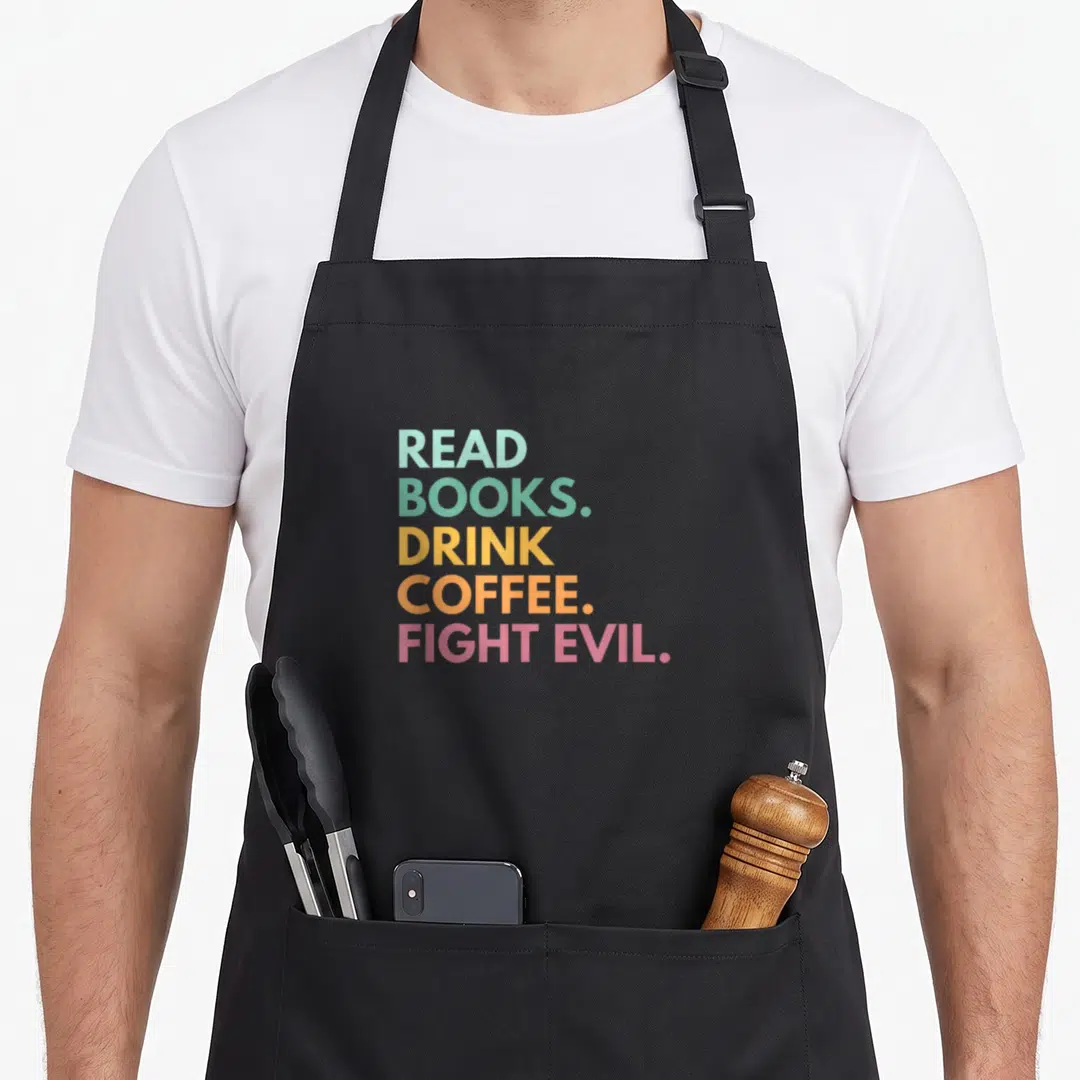 Fight coffee apron - Stacked colorful text reading READ BOOKS DRINK COFFEE FIGHT EVIL in blue, green, yellow, orange — shown on a black cotton canvas apron against a white background