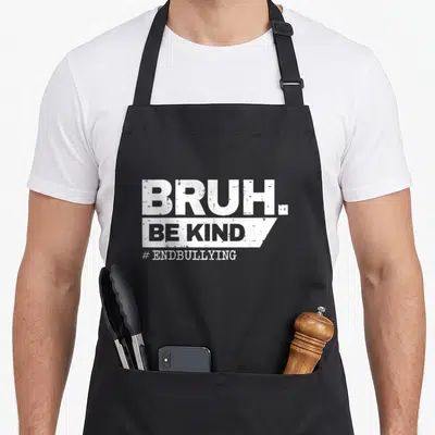 Kind unity apron - White stacked text BRUH BE KIND ENDBULLYING on grey background — shown on a black cotton canvas apron against a white background