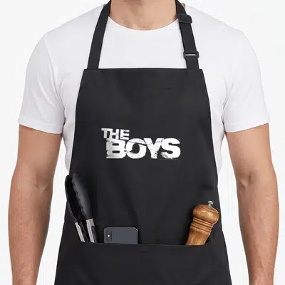 Show superhero apron - White distressed THE BOYS text stacked on two lines printed on black fabric — shown on a black cotton canvas apron against a white background