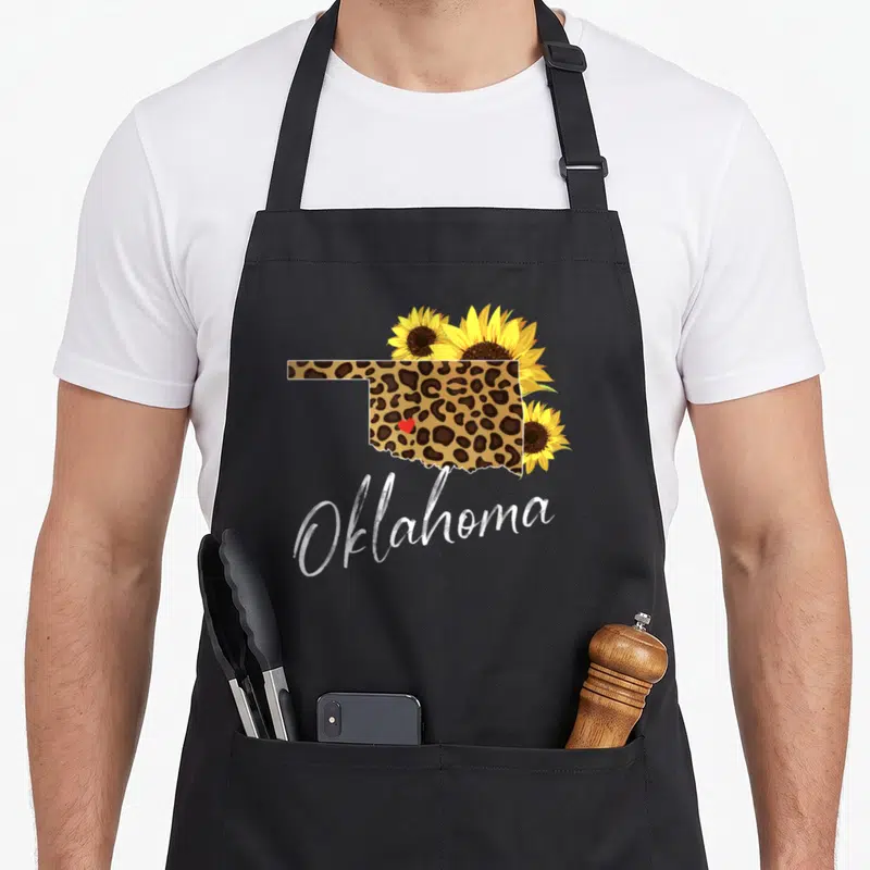 Oklahoma sunflower apron - Leopard print Oklahoma state map with yellow sunflowers and red heart — shown on a black cotton canvas apron against a white background