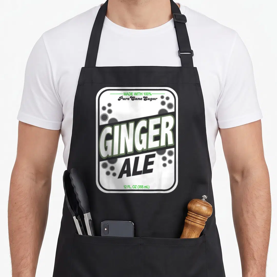 Ginger scotch ale apron - Retro soda can label print with stacked GINGER ALE text and grey bubbles — shown on a black cotton canvas apron against a white background