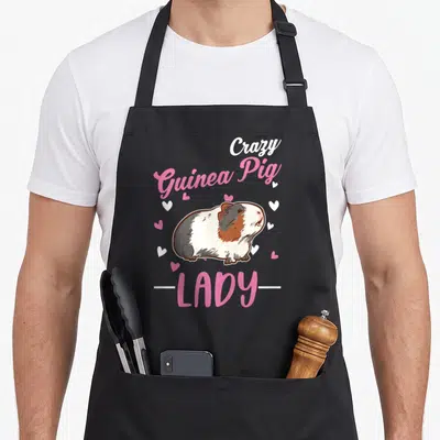 Cute animal crazy guinea lady apron - Cartoon guinea pig with pink and white hearts and text Crazy Guinea Pig LADY — shown on a black cotton canvas apron against a white background