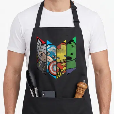 Chevron kawaii apron - Four cartoon heroes in red blue yellow green angled shards — shown on a black cotton canvas apron against a white background