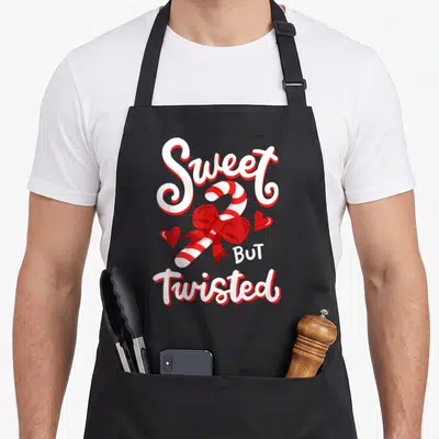 Twisted candy cane apron - Cartoon candy cane with red bow and hearts displaying Sweet BUT Twisted text — shown on a black cotton canvas apron against a white background