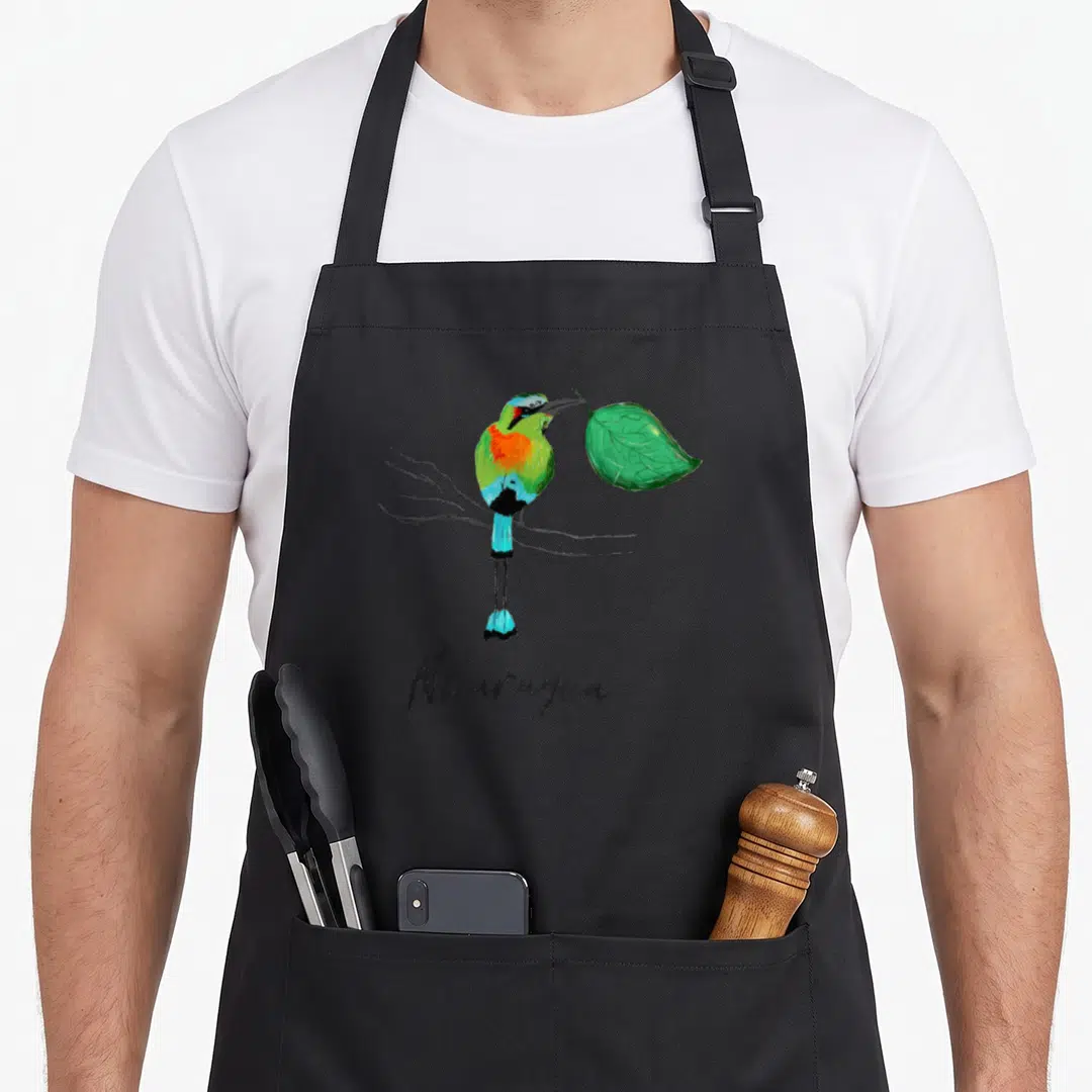 Nicaragua colorful aprons - Watercolor bird perched on branch holding green leaf with Nicaragua text below — shown on a black cotton canvas apron against a white background