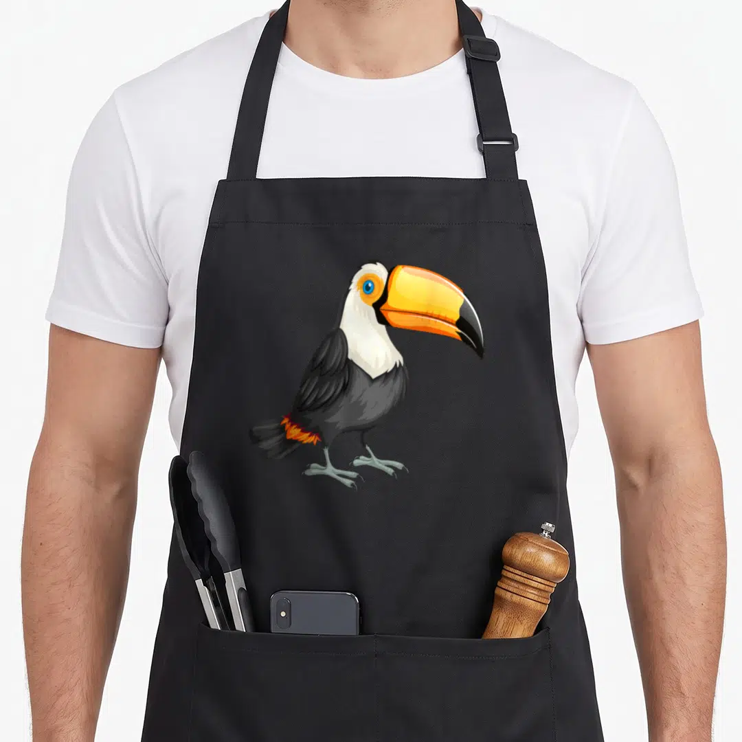 Toucan birds apron - Cartoon toucan with orange beak and black body on grey background — shown on a black cotton canvas apron against a white background