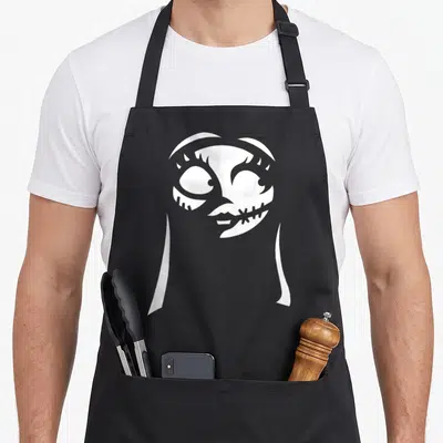Sally christmas apron - White silhouette of a stitched character head and shoulders against a grey background — shown on a black cotton canvas apron against a white background