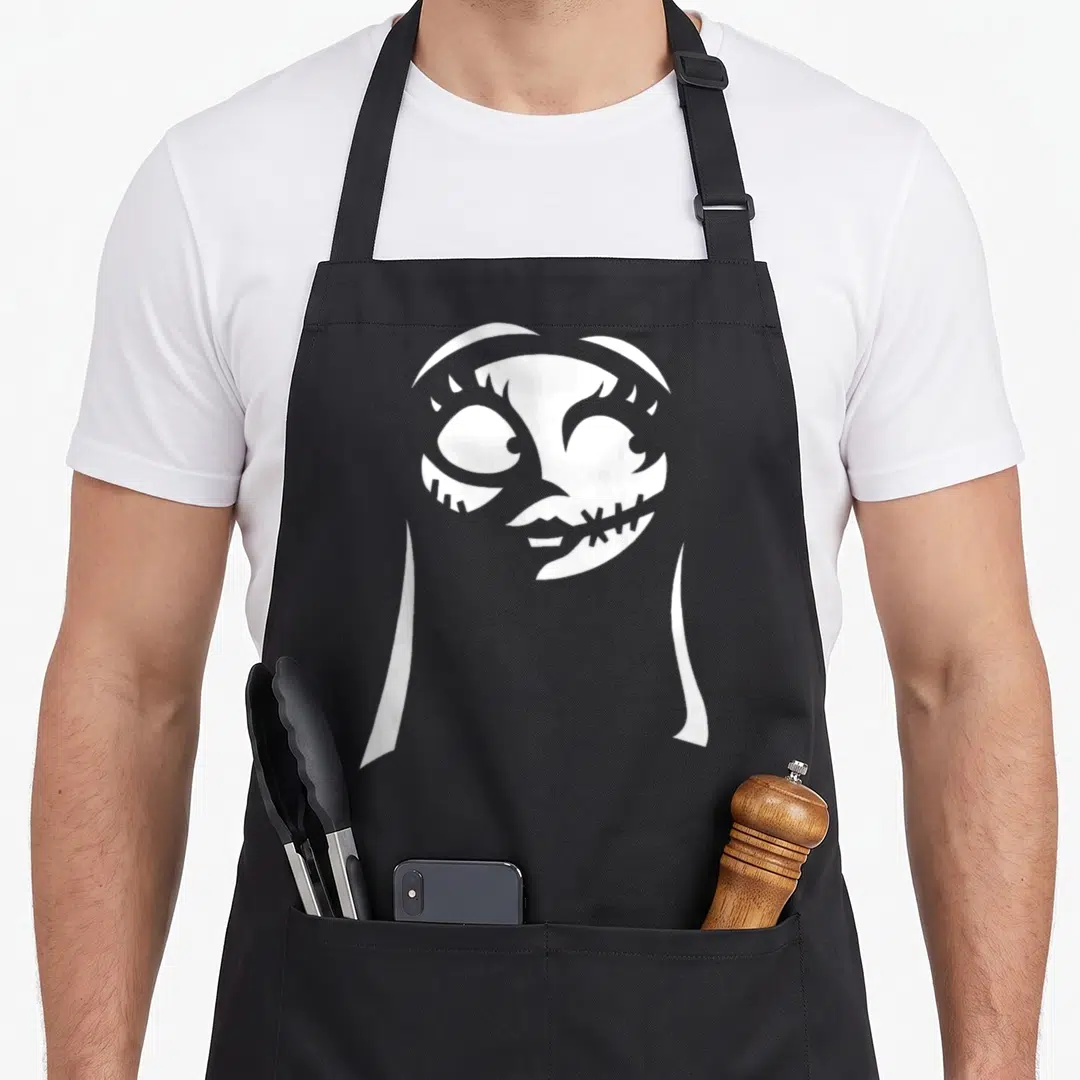 Sally christmas apron - White silhouette of a stitched character head and shoulders against a grey background — shown on a black cotton canvas apron against a white background