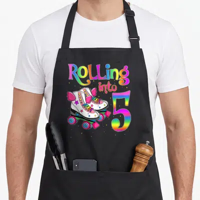 Roll roller skate turning apron - Rainbow Rolling into 5 text with pink winged roller skates and scattered stars — shown on a black cotton canvas apron against a white background