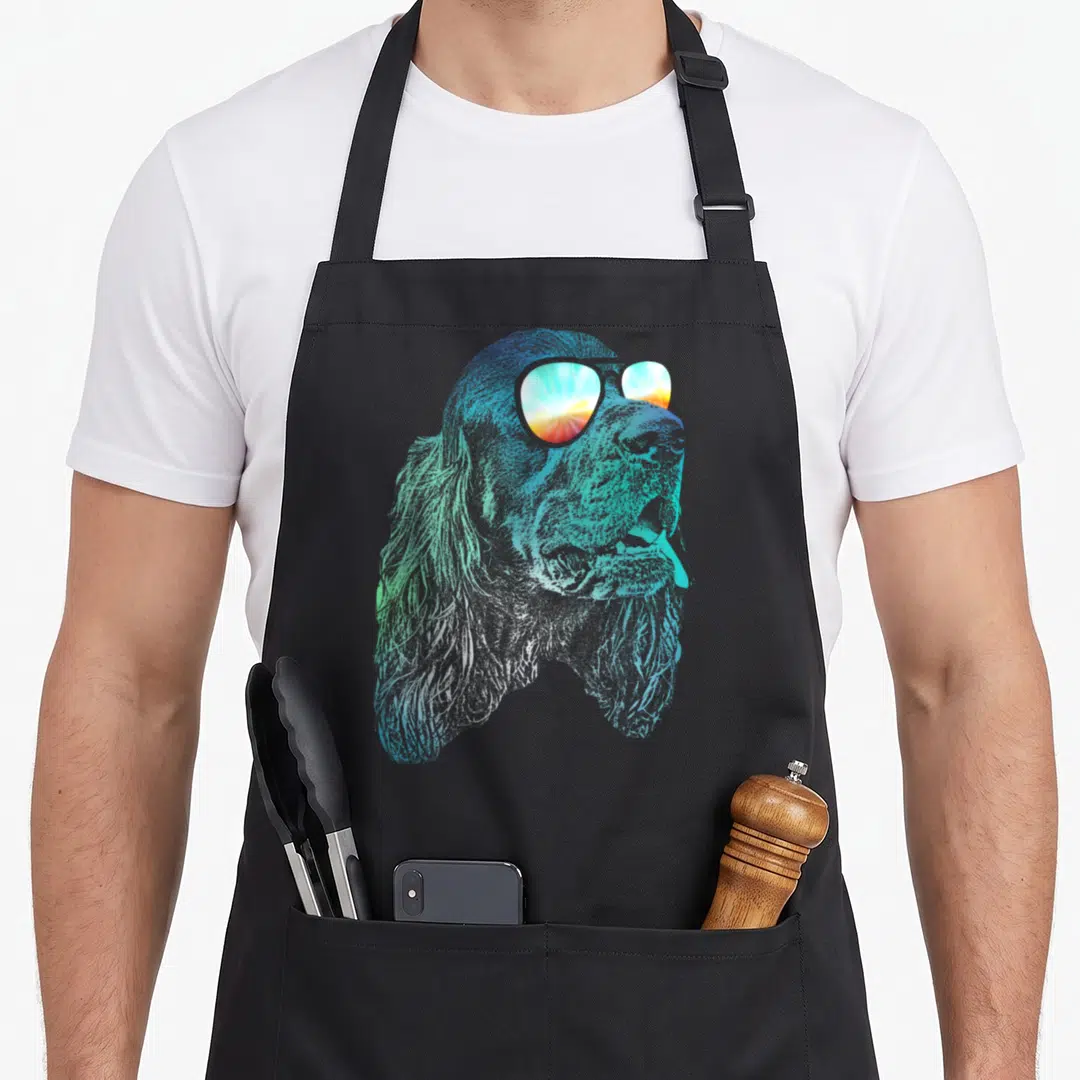 Gordon dog apron - Retro dog head illustration in blue and green wearing sunglasses with a sunset reflection — shown on a black cotton canvas apron against a white background