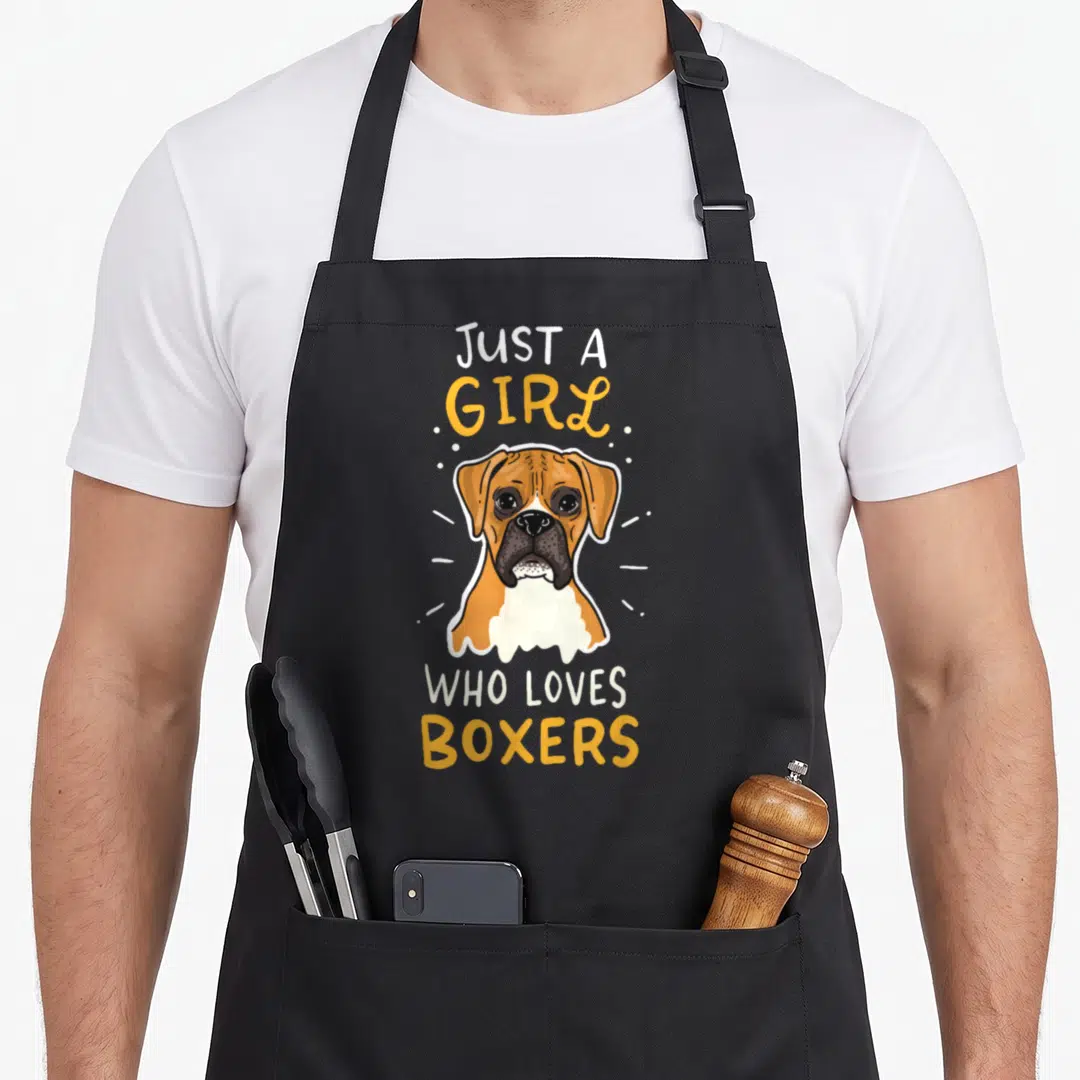 Breeder boxer dog apron - Cartoon boxer dog head framed by yellow and white text reading JUST A GIRL WHO LOVES BOXERS — shown on a black cotton canvas apron against a white background