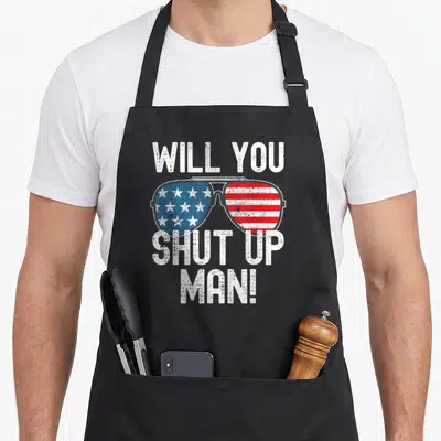 Shut debate humor apron - Distressed sunglasses with US flag lenses and text Will You Shut Up Man — shown on a black cotton canvas apron against a white background