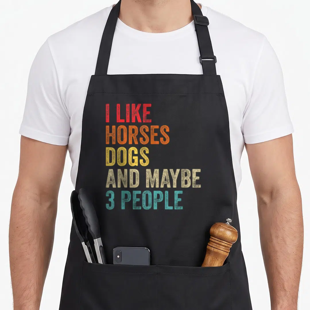 Horse dog apron - Stacked colorful text reading I Like Horses Dogs And Maybe 3 People in red orange yellow beige teal — shown on a black cotton canvas apron against a white background
