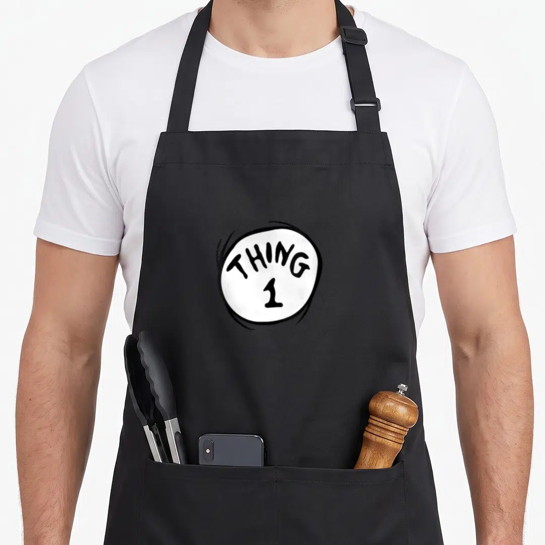 Emblem officially apron - White circle with sketchy black outline containing the text THING 1 in a cartoon font — shown on a black cotton canvas apron against a white background