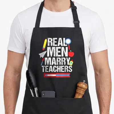 Proud teacher pocket apron - Real Men Marry Teachers text with pencil, apple, glue, and paper plane in distressed style — shown on a black cotton canvas apron against a white background