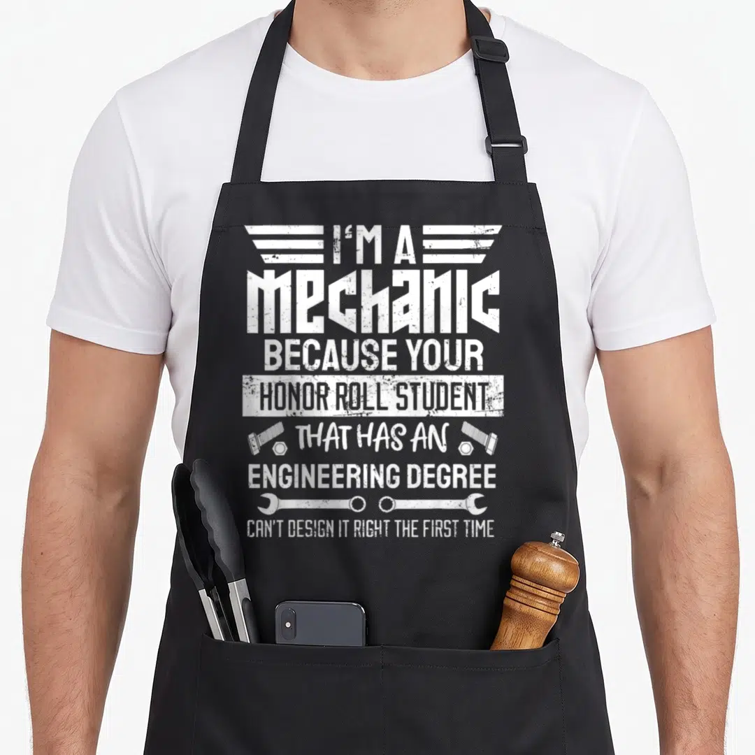 Diy garage apron - White distressed text reading I'm a mechanic with two wrenches and screws — shown on a black cotton canvas apron against a white background