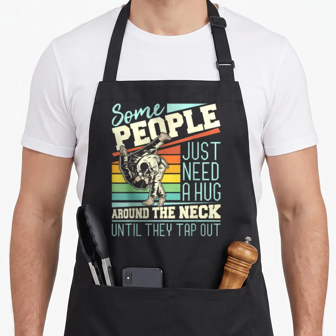 Hug brazilian apron - Retro martial artist graphic with colored stripes and text about hugging until tap out — shown on a black cotton canvas apron against a white background