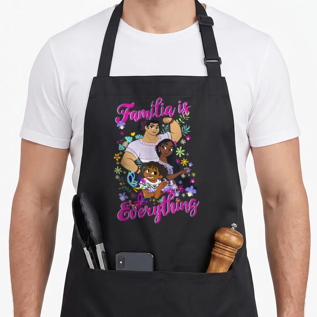 Familia group shot apron - Three women surrounded by pink, purple, green, and white flowers with text reading Familia — shown on a black cotton canvas apron against a white background