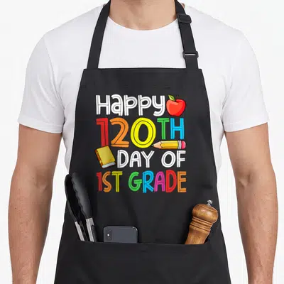 120th teacher apron - Stacked text Happy 120TH DAY OF 1ST GRADE with apple pencil book in red orange yellow green blue — shown on a black cotton canvas apron against a white background