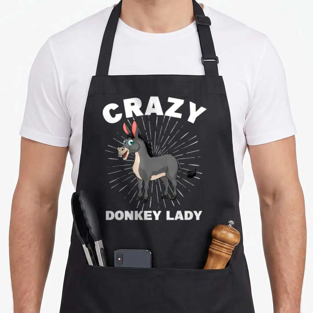 Zoo farmer apron - Cartoon grey donkey with white sunburst and Crazy Donkey Lady text — shown on a black cotton canvas apron against a white background
