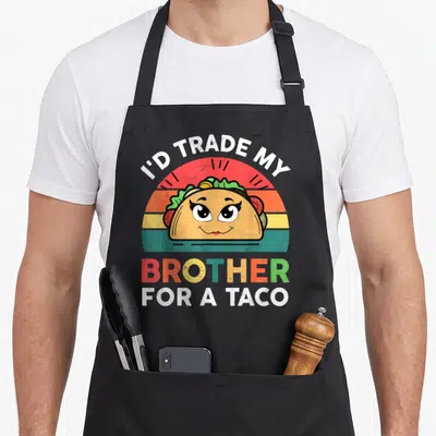 Trade mexican apron - Cartoon taco with eyes on retro sunset, text reads I'd Trade My Brother For A Taco — shown on a black cotton canvas apron against a white background