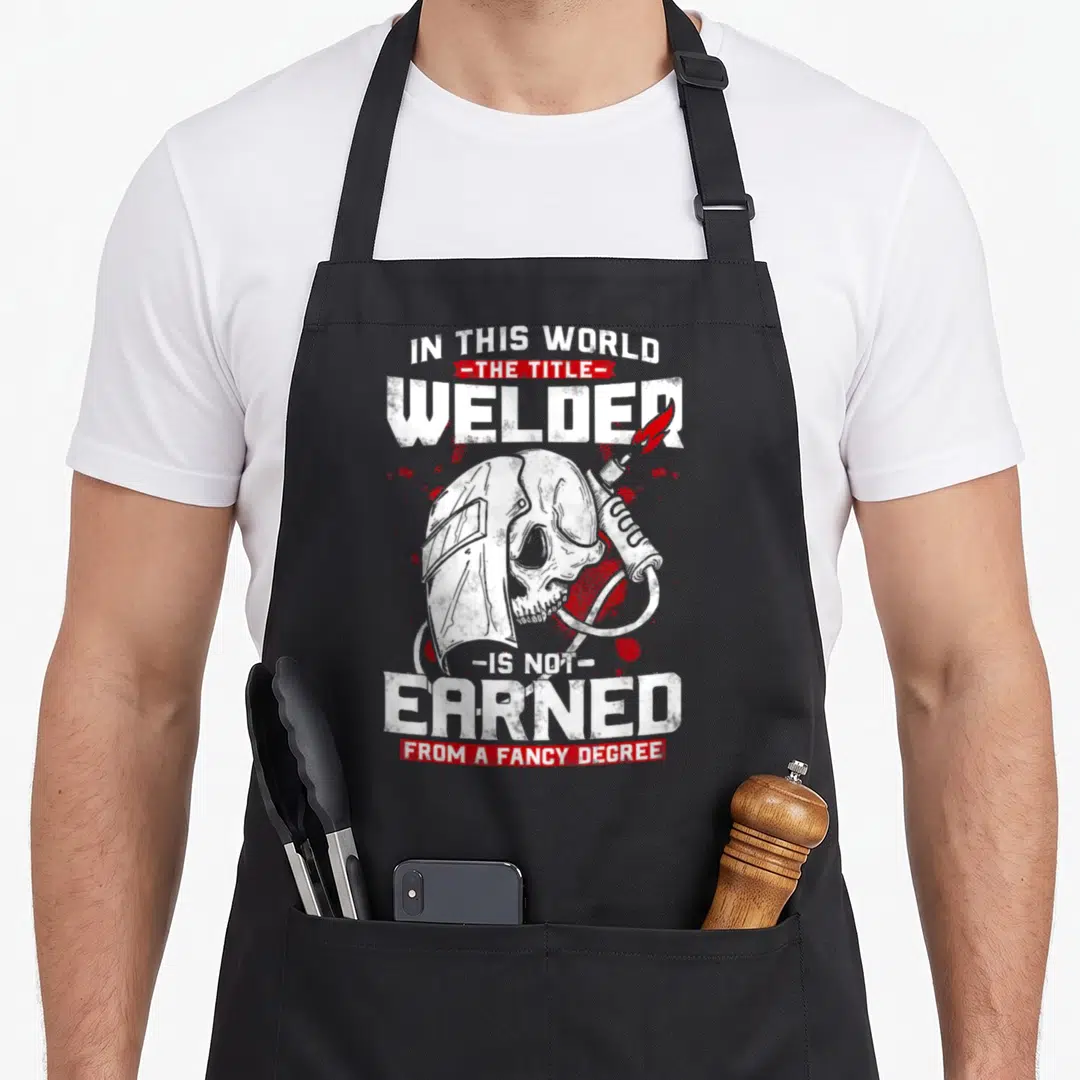 Tittle welder dad apron - Distressed skull wearing welding helmet with torch and white text on black background — shown on a black cotton canvas apron against a white background