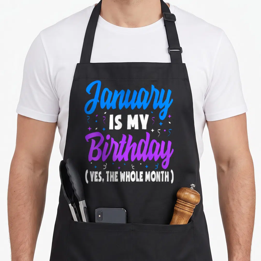 January whole birthday apron - Stacked blue purple and white text reading January is my birthday yes the whole month — shown on a black cotton canvas apron against a white background