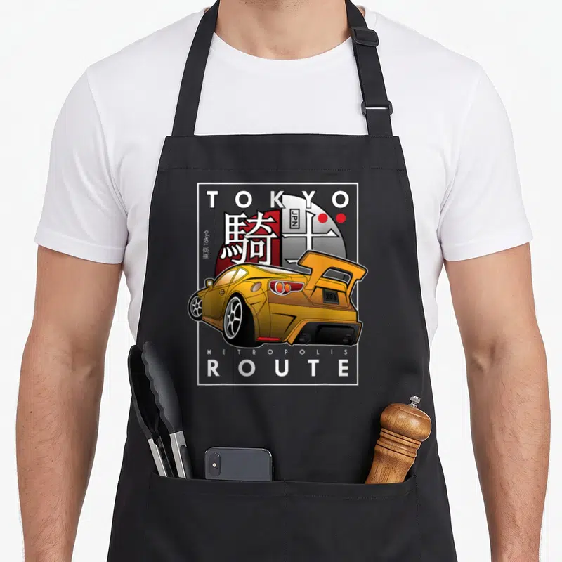 Tokyo design imports vintage apron - Yellow modified car with Tokyo Metropolis Route text and red sun background — shown on a black cotton canvas apron against a white background