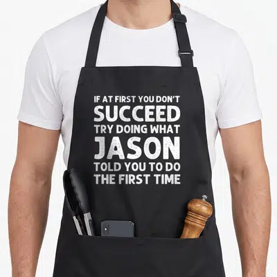 Jason christmas apron - White distressed typography reading If At First You Don't Succeed Try Doing What Jason Told You — shown on a black cotton canvas apron against a white background