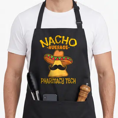 Nacho pharmacist apron - Cartoon nacho chip wearing a sombrero and mustache with text reading Nacho Average Pharmacy — shown on a black cotton canvas apron against a white background