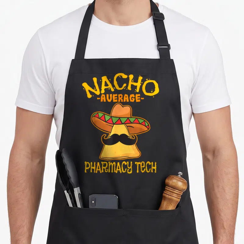 Nacho pharmacist apron - Cartoon nacho chip wearing a sombrero and mustache with text reading Nacho Average Pharmacy — shown on a black cotton canvas apron against a white background