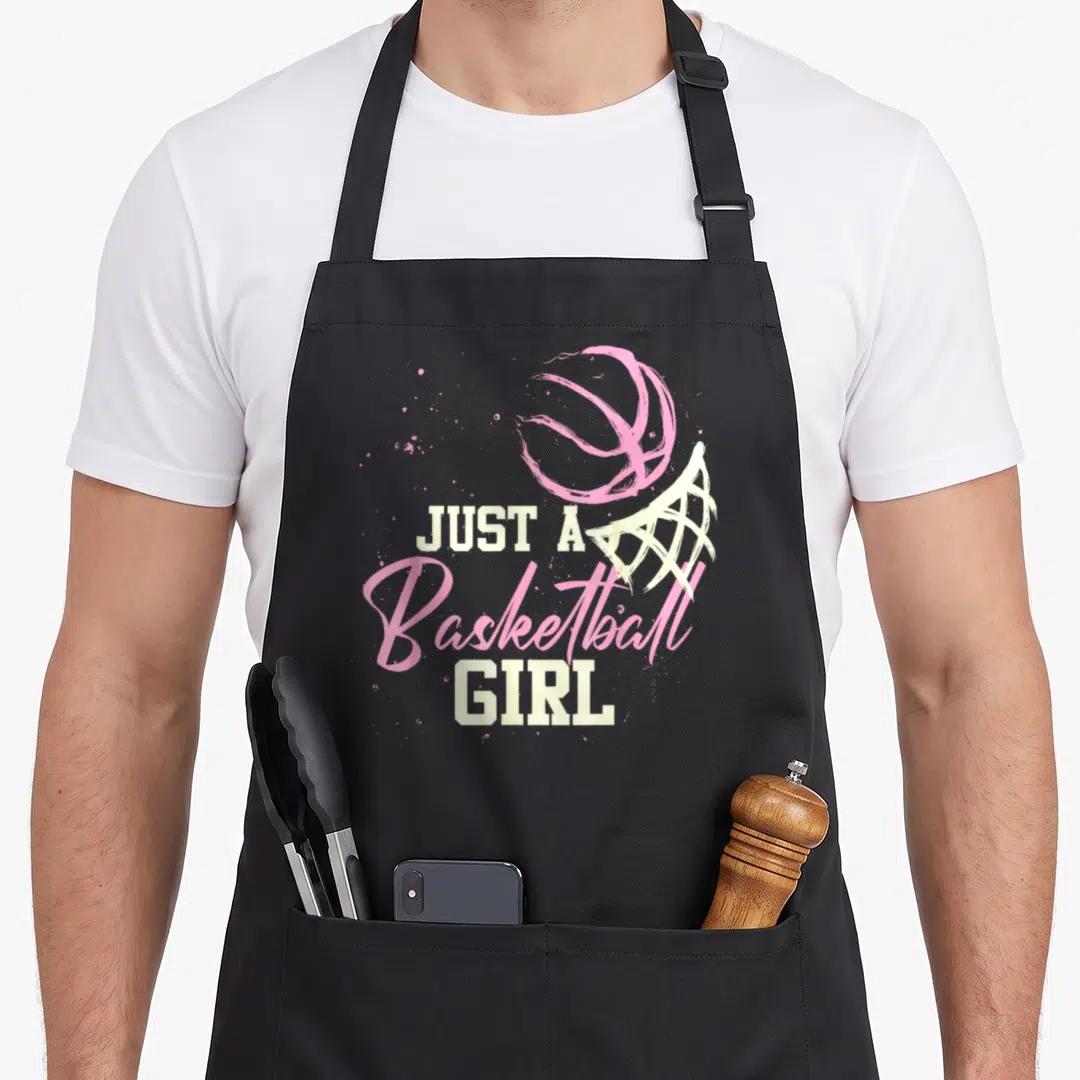 Vintage player basketball apron - Pink basketball and cream hoop with stacked Just A Basketball Girl text and splatters — shown on a black cotton canvas apron against a white background