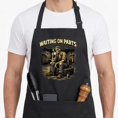 Repair auto mechanic apron - Skeleton mechanic sitting on tire holding coffee mug under arched text reading waiting — shown on a black cotton canvas apron against a white background