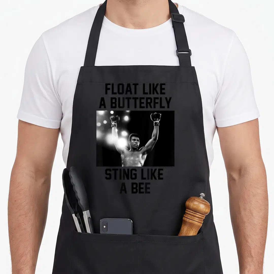 Ali bee apron - Muhammad Ali photo with Float Like A Butterfly Sting Like A Bee text — shown on a black cotton canvas apron against a white background