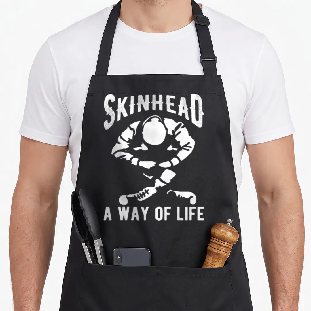 Skinhead ideas apron - White arched text SKINHEAD above sitting silhouette and crossed boots with A WAY OF LIFE below — shown on a black cotton canvas apron against a white background