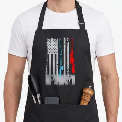 Shotgun fishing aprons - Distressed white flag with blue fishing rod red rifle and white antlers — shown on a black cotton canvas apron against a white background
