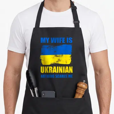 Pride wife apron - Distressed blue and yellow flag with text MY WIFE IS UKRAINIAN NOTHING SCARES ME — shown on a black cotton canvas apron against a white background
