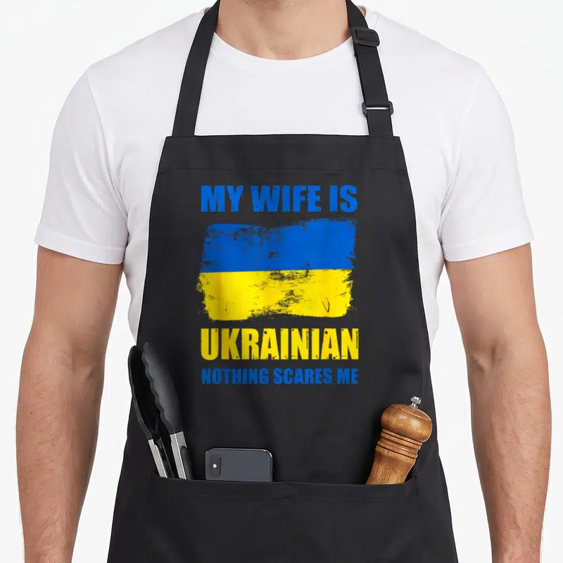 Pride wife apron - Distressed blue and yellow flag with text MY WIFE IS UKRAINIAN NOTHING SCARES ME — shown on a black cotton canvas apron against a white background