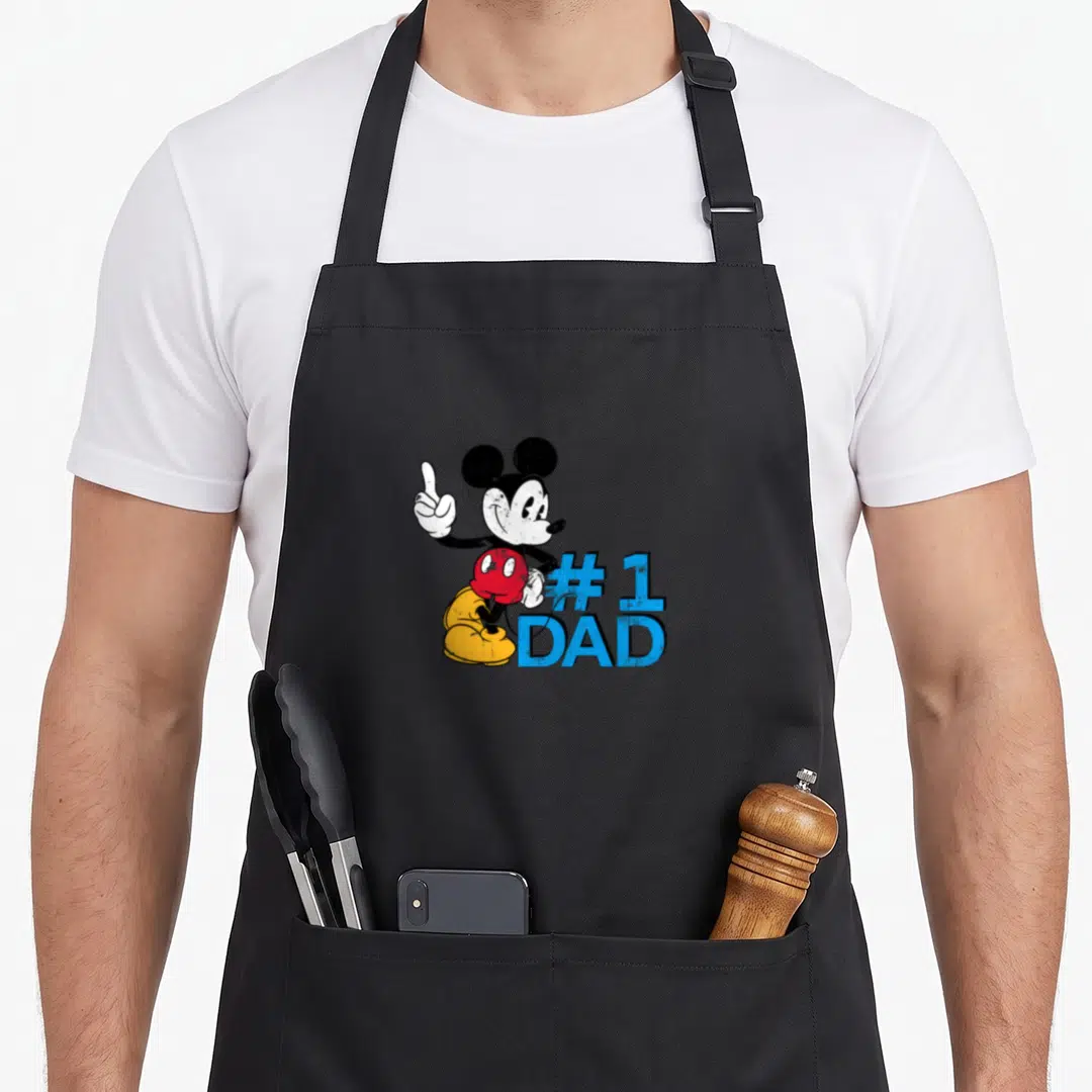 Father day apron for chefs - Mickey Mouse pointing up beside blue #1 DAD text on black background — shown on a black cotton canvas apron against a white background