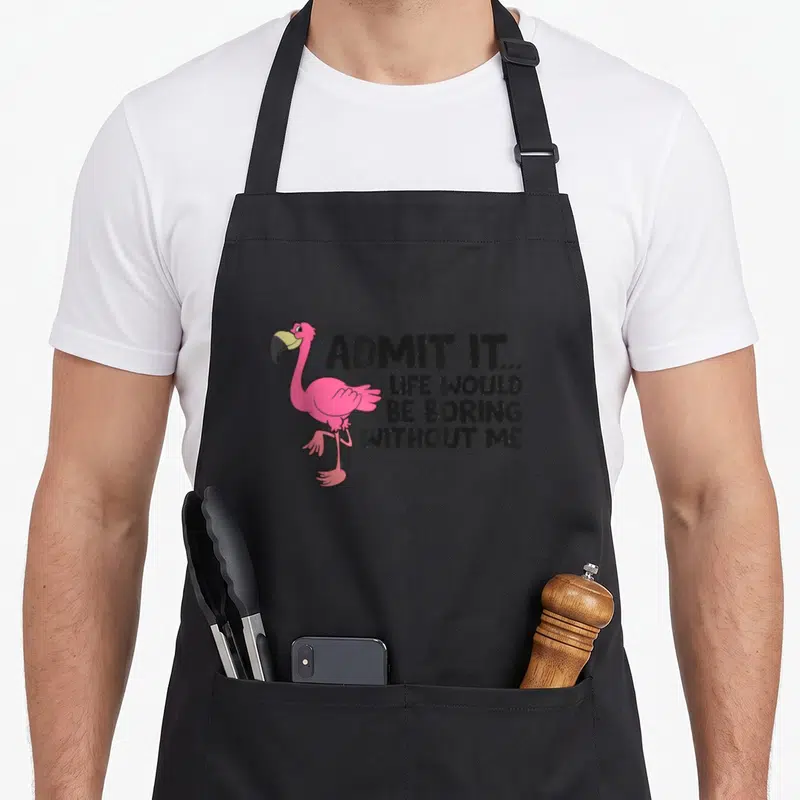 Admit flamingo apron - Pink cartoon flamingo standing next to black text admitting life would be boring without me — shown on a black cotton canvas apron against a white background