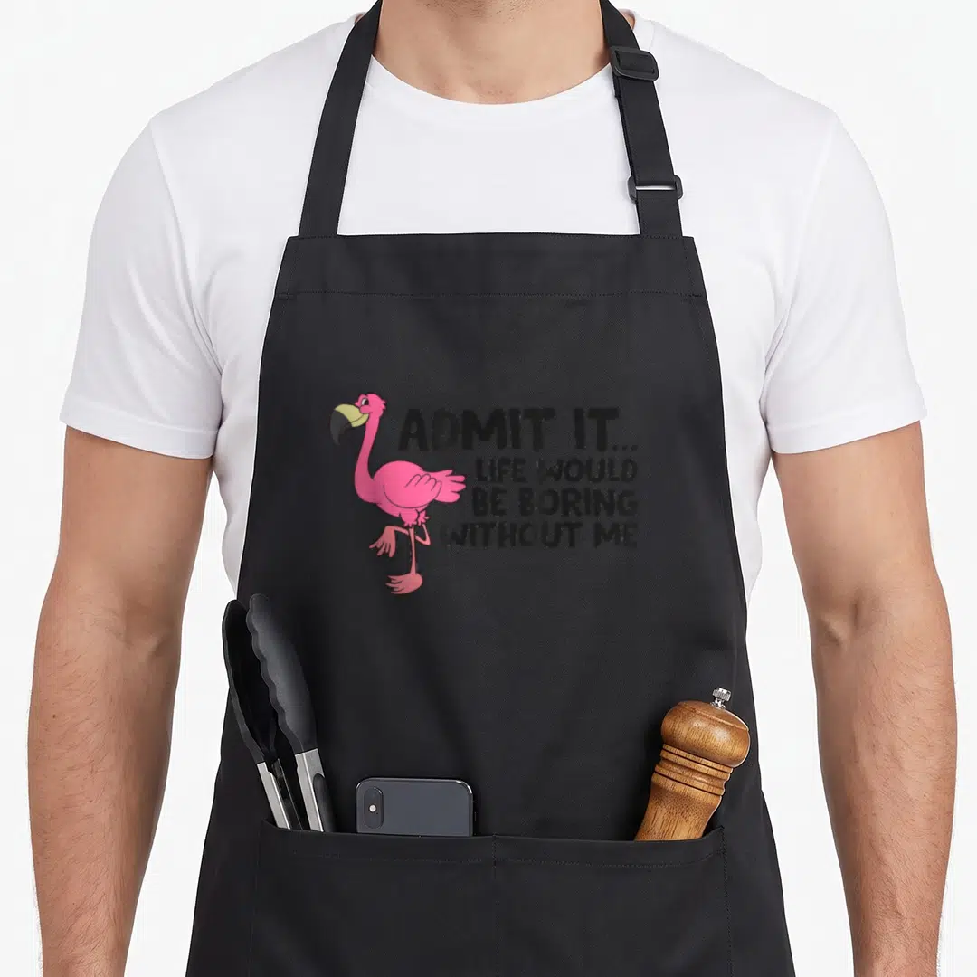 Admit flamingo apron - Pink cartoon flamingo standing next to black text admitting life would be boring without me — shown on a black cotton canvas apron against a white background