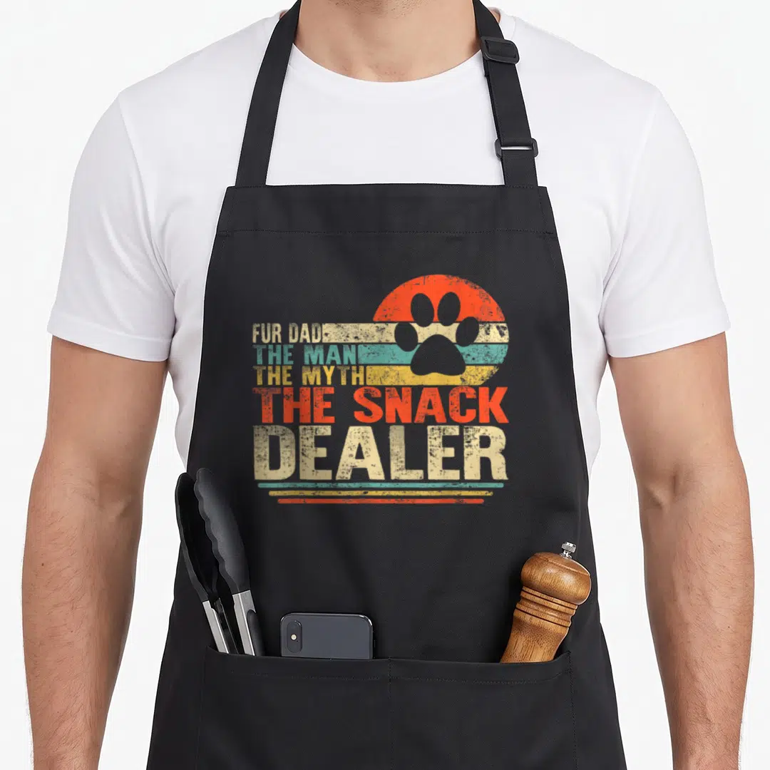 Fur dog dad apron - Retro striped paw print with FUR DAD THE SNACK DEALER text in distressed beige teal yellow orange — shown on a black cotton canvas apron against a white background